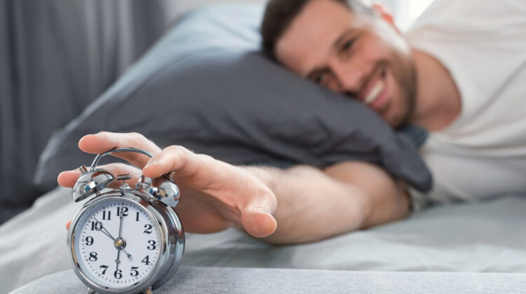 man waking up shutting off alarm clock