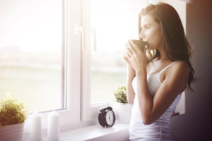 woman drinking coffee by window after waking up