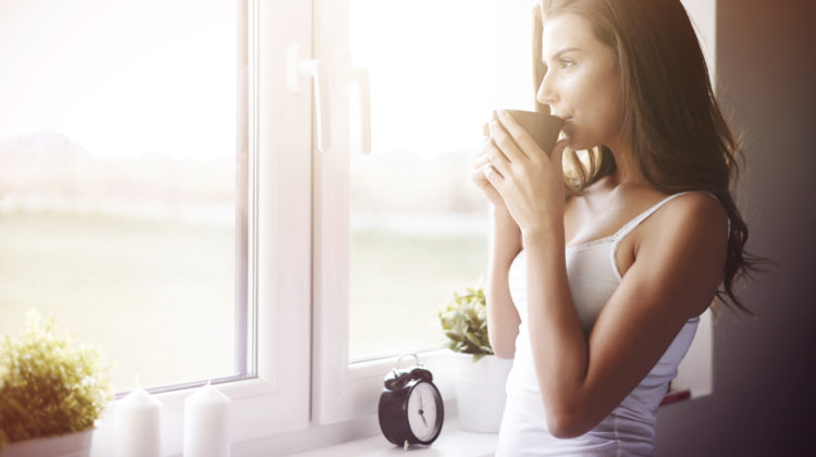 woman drinking coffee by window after waking up